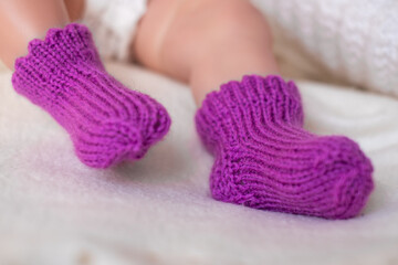 Cute baby wearing handmade purple knitted booties, resting peacefully on a soft blanket indoors