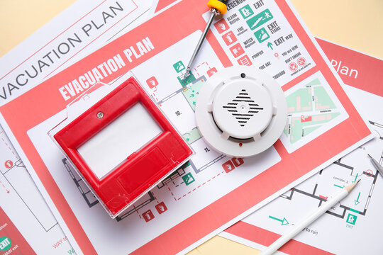 Modern smoke detector with fire call point and evacuation plans on yellow background