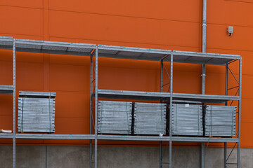 Stacked metal shelves against an orange wall in a warehouse.