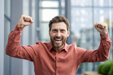 Happy man with raised fists celebrating success in office environment. Joyful expression, relaxed...