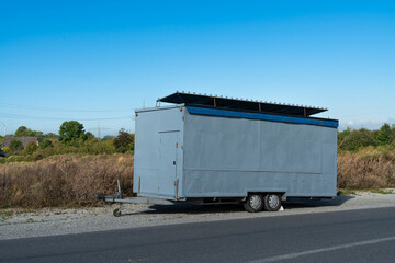 Gray trailer parked along a rural road under a clear blue sky