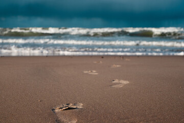 Tranquil beach scene with footprints leading toward the ocean under a dramatic sky at sunset