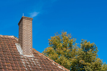 Chimney on a rustic roof surrounded by autumn foliage in daylight