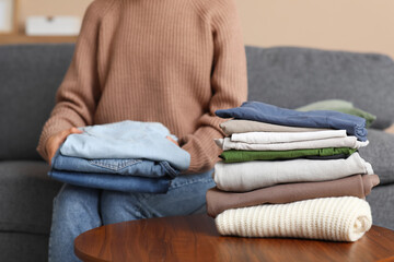 Young woman w stacks of clothes at home, closeup
