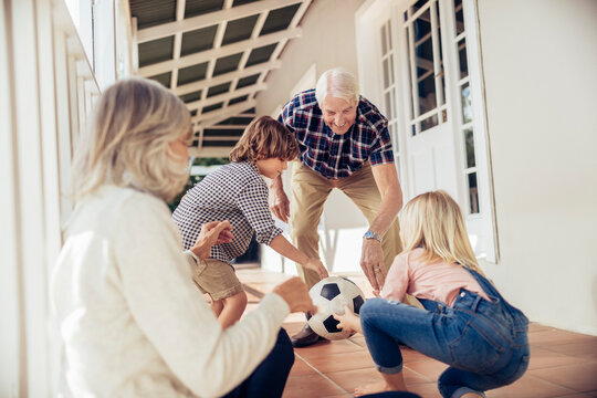 Grandparents and grandchildren playing with soccer ball on house porch - Powered by Adobe