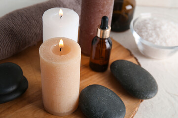 Burning candles, essential oil and spa stones on light background