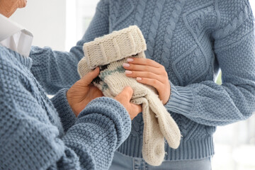 Senior woman giving knitted socks to her granddaughter in kitchen at home, closeup