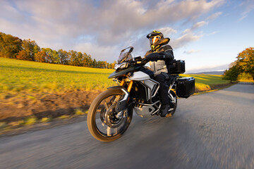Driver riding motorcycle on empty road during sunset, autumn mountains