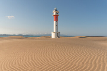 Lighthouse of Delta del Ebro among the Fangar beach dunes at sunset in a sunny day