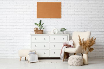 Armchair, pouf, pampas grass, frame and chest of drawers near white wall in room