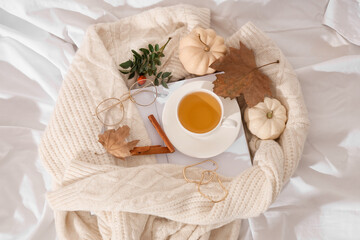 Composition with cup of green tea, notebook, sweater and autumn leaves on light fabric as background