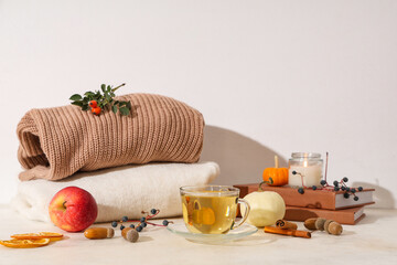 Autumn composition with cup of green tea, notebooks and sweaters on table near white wall