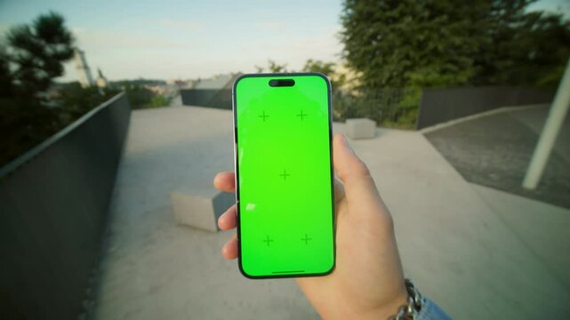 Footage of male hand holding mobile phone in vertical position while chatting with girlfriend. Young man walking through bridge in evening outdoors. Blurred background of beautiful ancient city