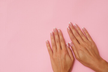 Beautiful feminine hands with French manicure on pastel pink background.