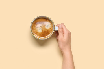 Female hand with cup of coffee on beige background