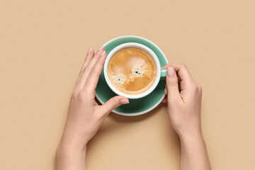 Female hands with cup of coffee on beige background