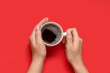 Female hands with cup of coffee on red background