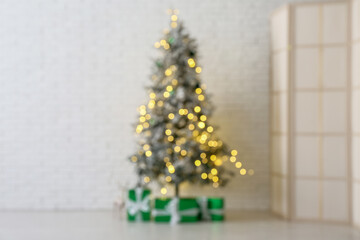 Blurred view of decorated Christmas tree with glowing lights and gift boxes near white brick wall