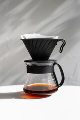 Brewing fresh coffee with a pour-over method using a black filter cone and glass carafe on a minimalist countertop during daylight