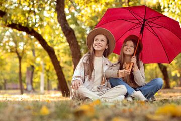 Cute girls with umbrella sitting in park on autumn day