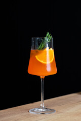 A refreshing orange cocktail garnished with herbs in a tall glass on a wooden table in a dimly lit setting