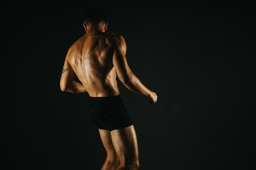 Naklejka premium Fit man displaying his strong back muscles in a low light studio environment, showcasing fitness and strength.