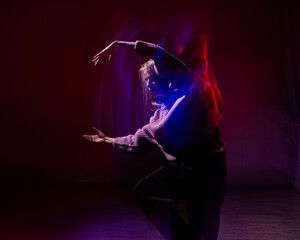 A young woman dances contemporary dances in blue and red light. Long exposure photo. 