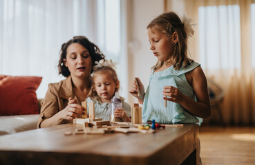 A mother and her two daughters engaging in creative play with wooden blocks at home. The warm, cozy scene captures family bonding and childhood development in a relaxed environment.