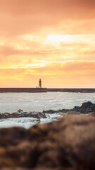Porto lighthouse silhouette against golden sunset sky with dramatic waves and rocky shore