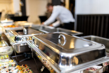 Catering setup with stainless steel trays filled with food at an event, showcasing a variety of dishes prepared for guests