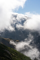 Stunning mist-covered mountain landscape with thick clouds rolling through a sunlit valley. Concept of untouched wilderness, serene nature, and outdoor adventure. High quality photo