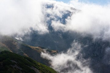 Spectacular view of a misty mountain valley covered with thick clouds on a sunny day. Concept of pristine nature, wilderness, and alpine adventure. High quality photo