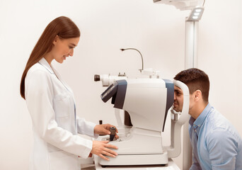 Medical Center. Lady ophthalmologist checking eye vision of handsome young man in modern clinic,...