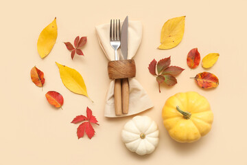 Stylish cutlery with fresh pumpkins and autumn leaves on beige background