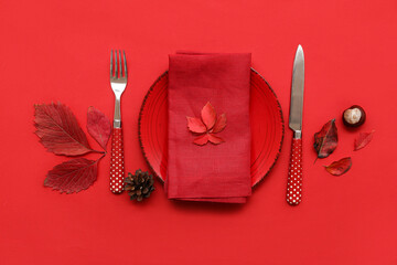 Beautiful table setting with pine cone, chestnut and autumn leaves on red background