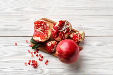 Board with fresh ripe pomegranates and seeds on white wooden background