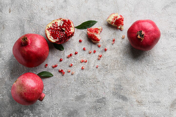 Fresh ripe pomegranates with seeds and leaves on grey background