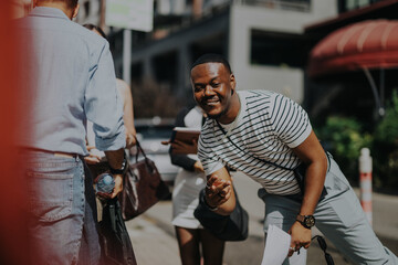 Group of business people engage cheerfully outdoors, enjoying a sunny day in a lively urban area. The atmosphere is friendly and relaxed, showcasing positive interactions and professional camaraderie.