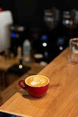A freshly crafted latte sits on a wooden counter in a bustling coffee shop with blurred backgrounds during the afternoon hours