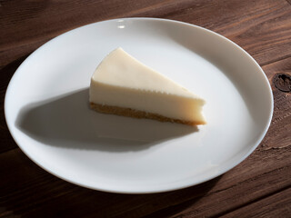 delicious cheesecake on a white plate. Wooden background, hard shadows