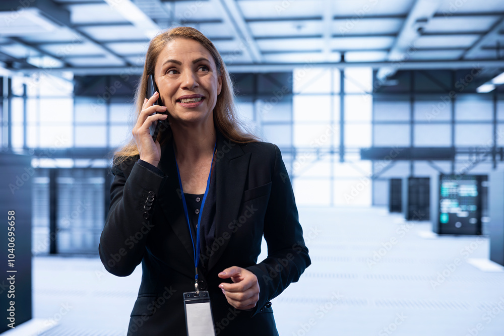 Poster smiling person overseeing operations in cutting edge data center, coordinating tasks during telephon