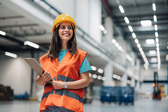 Female warehouse worker holding clipboard smiling at camera