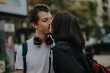 A young couple shares a tender kiss outdoors, radiating affection amidst an urban backdrop. The casual setting highlights youthful love and connection in the bustling city environment.