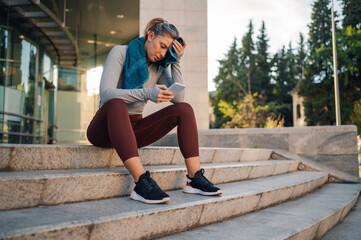Fototapeta premium Tired female athlete checking her phone after outdoor training session
