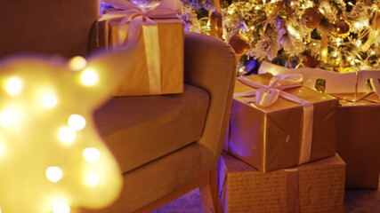 Christmas presents wrapped in gold paper and tied with ribbons are placed under a decorated christmas tree with warm lights