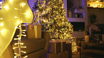 Decorated christmas tree is illuminating a cozy living room with wrapped gifts on the floor and a glowing reindeer decoration