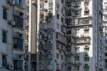 Urban density: weathered facade of an older high-rise apartment building with multiple air conditioning units in an Asian metropolis. A populated residential neighborhood in Macau, China.