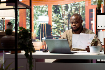 Obraz premium Freelancer at home conducting business analysis and creating detailed financial reports on a modern laptop. Remote working professional man manages startup projects strategies.