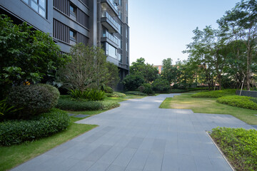 A modern residential building features a sleek, minimalist design with a landscaped courtyard,including a paved pathway winding through lush green lawns and shrubs in the communal public outdoor space