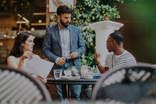 A diverse group of business professionals brainstorms and strategizes during a meeting in a stylish coffee shop. The scene depicts collaboration and innovation in a modern setting.